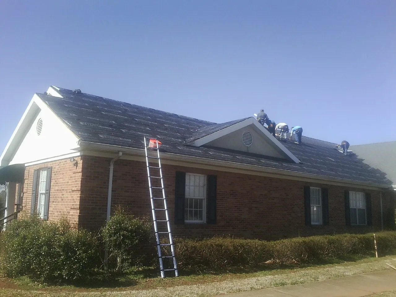 Crew tearing shingles off a brick ranch roof with a ladder set — Emergency Roof Repair work by our crew in Ringtown