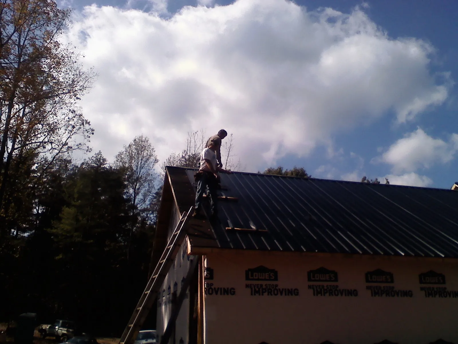 Roofer fastening dark metal panels high against a cloudy sky, from a Roof Inspection job in Ringtown